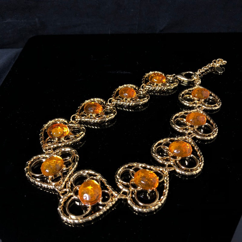 Vintage-style jewelry, including necklaces and earrings, featuring orange jelly resin inlays, a hollowed-out heart pendant design, and an elegant aesthetic