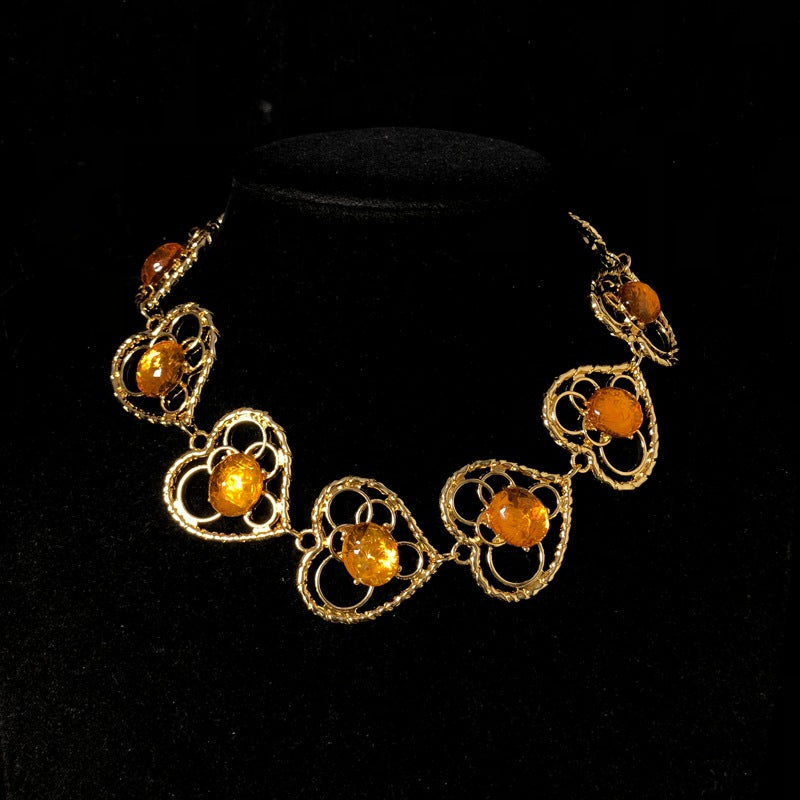 Vintage-style jewelry, including necklaces and earrings, featuring orange jelly resin inlays, a hollowed-out heart pendant design, and an elegant aesthetic