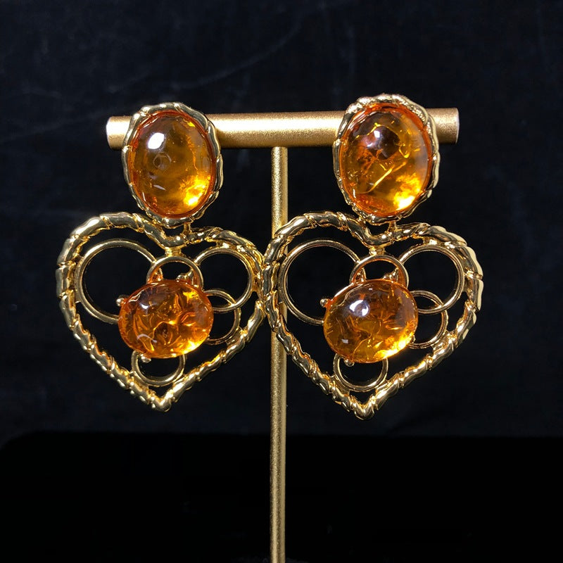 Vintage-style jewelry, including necklaces and earrings, featuring orange jelly resin inlays, a hollowed-out heart pendant design, and an elegant aesthetic